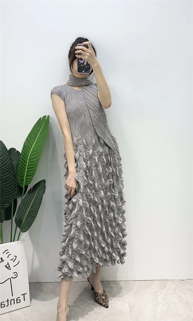 Woman wearing a gray dress with ruffled skirt against a white wall.