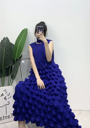 Person wearing a blue ruffled dress sitting on a chair with a white wall and plant in the background.