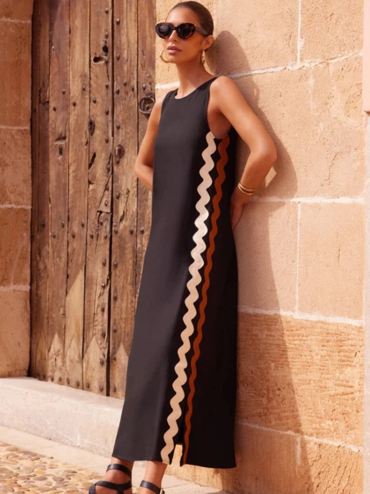 Woman wearing a black sleeveless dress with zigzag pattern against a stone wall.