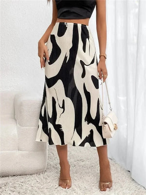 A woman wearing a black and white graphic print pleated long skirt with a high waist, midi length, and elastic band, paired with a crop top and beige accessories.