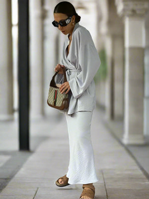 Woman in a white outfit holding a patterned handbag, standing indoors.