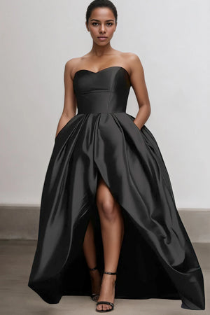 Woman wearing a black strapless gown with a high-low hem on a plain background