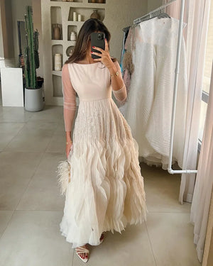 Woman taking a mirror selfie wearing a long, light-colored dress with feather details.