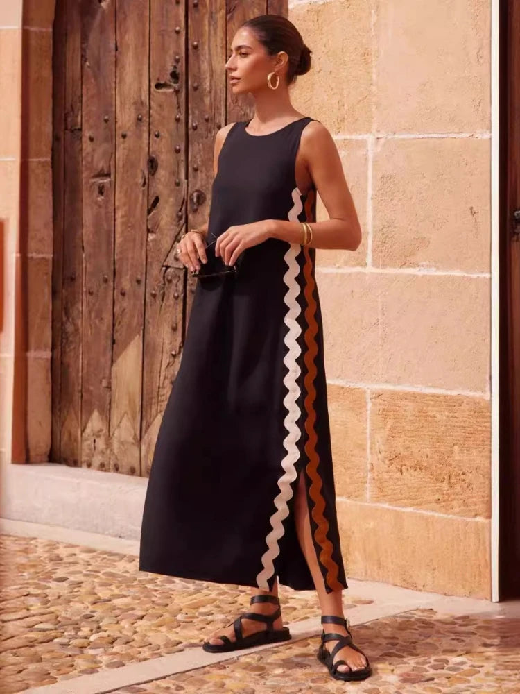 Woman wearing a black dress with a white zigzag pattern standing in front of a stone wall.