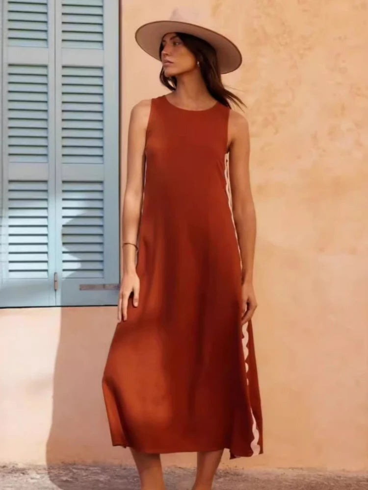 Woman wearing a rust-colored dress and beige hat against a peach wall.