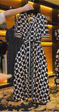 A checkered black and white midi dress with a V-neck, short sleeves, and lace-up detail at the waist displayed in a retail setting.