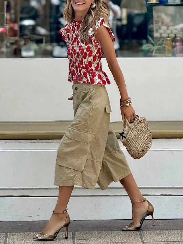 Woman wearing a red floral top and beige skirt with a straw bag, standing on steps.