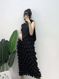Person wearing a black sleeveless top and ruffled black skirt against a white wall.