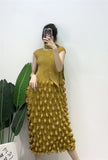 Person wearing a mustard yellow textured dress against a white wall with green leaves.