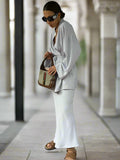 Woman in a white outfit holding a patterned handbag, standing indoors.