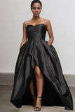 Woman wearing a black strapless gown with a high-low hem on a plain background