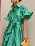 Woman wearing a green dress with ruffled sleeves against a neutral background