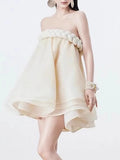 Woman wearing a strapless beige dress with floral embellishments on a white background